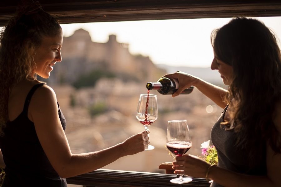 Dos amigas sirven vino tinto con Alquézar al fondo